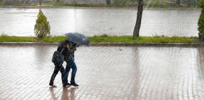 Two travelers walking under heavy rain with an umbrella