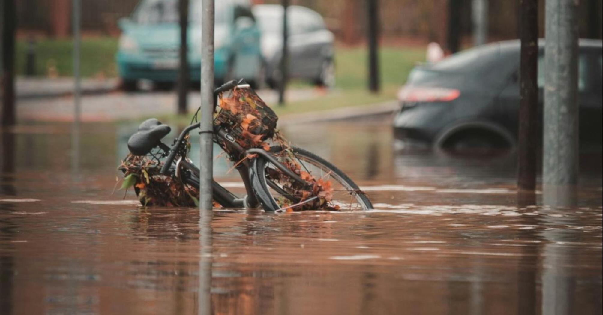 Flooded street with a bicycle partially submerged near a pedestrian crossing sign