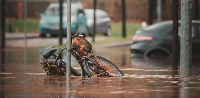 Flooded street with a bicycle partially submerged near a pedestrian crossing sign