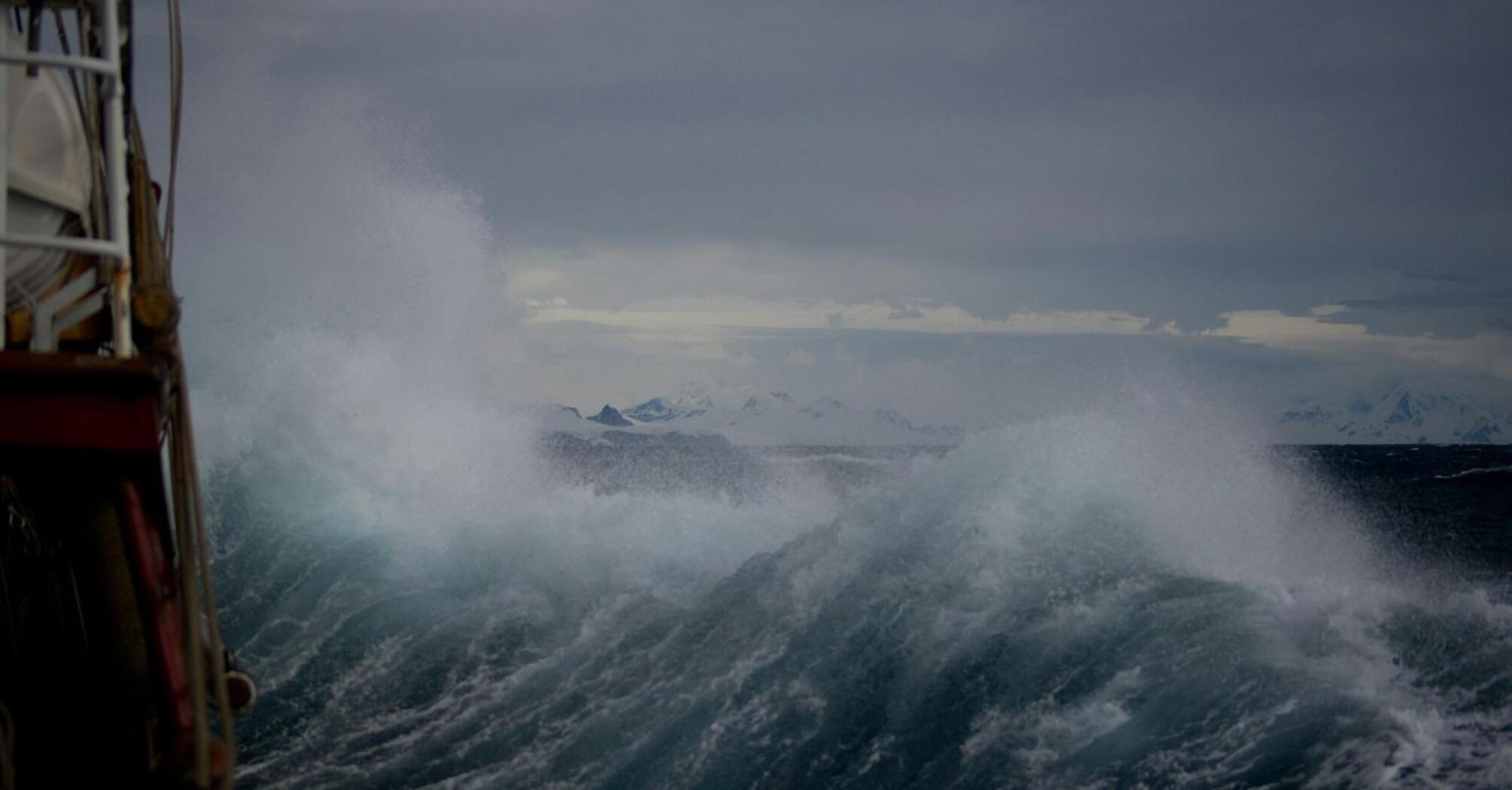 Large storm waves crashing near a vessel under dark skies
