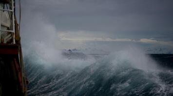 Large storm waves crashing near a vessel under dark skies