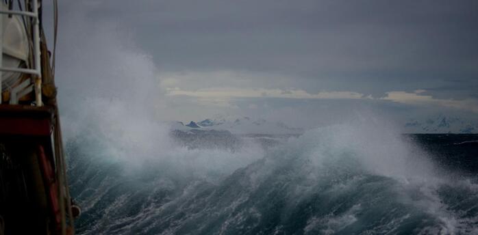 Large storm waves crashing near a vessel under dark skies