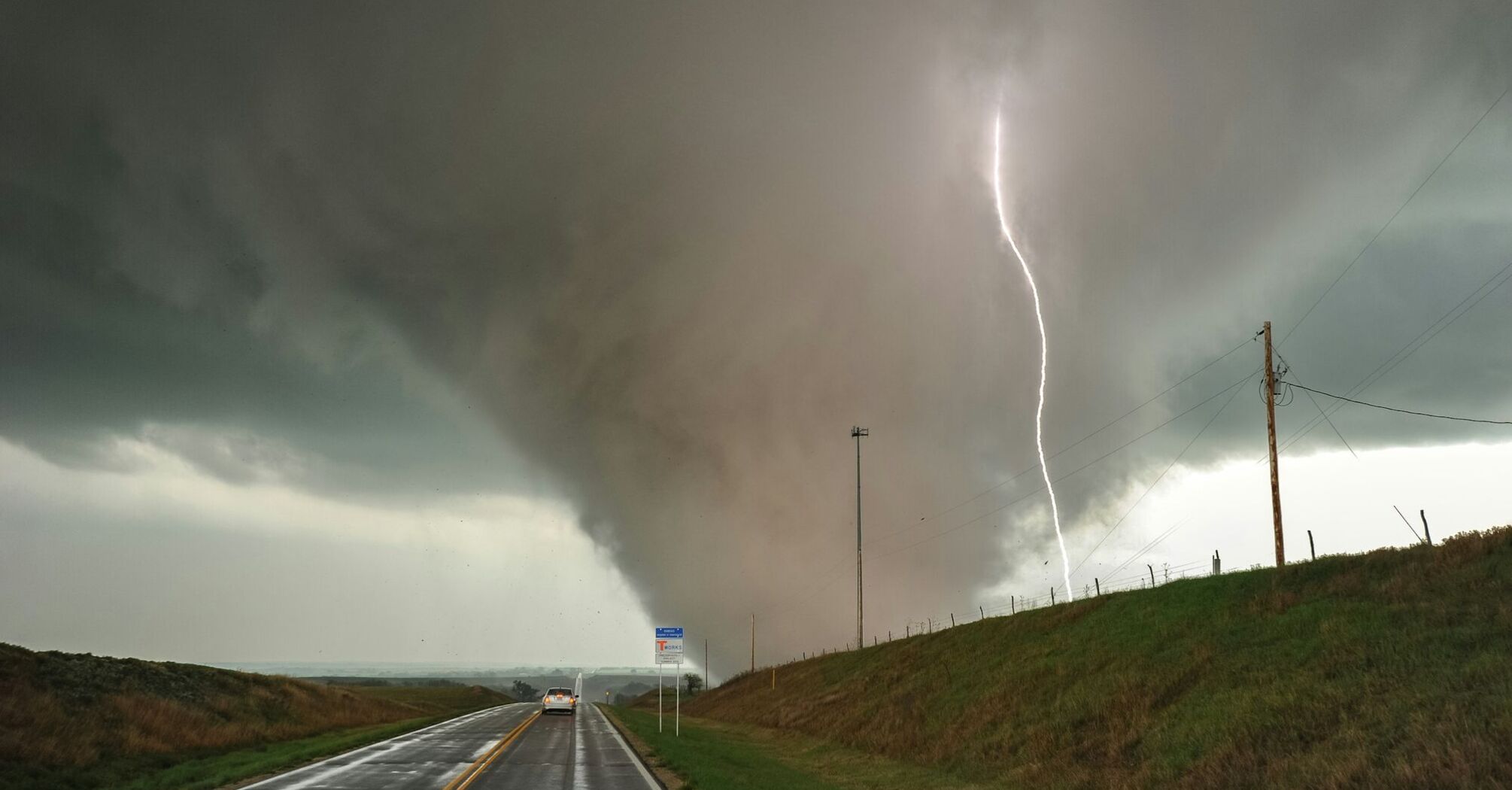 Severe storm conditions with a tornado and lightning over a rural road