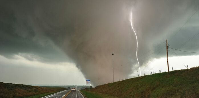 Severe storm conditions with a tornado and lightning over a rural road