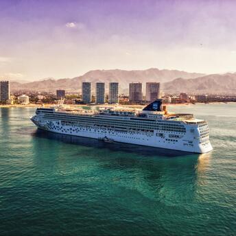 Norwegian Cruise Line ship sailing near a coastal city