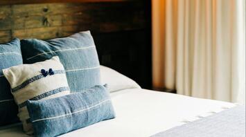 A neatly arranged hotel room with soft lighting and blue-toned bedding