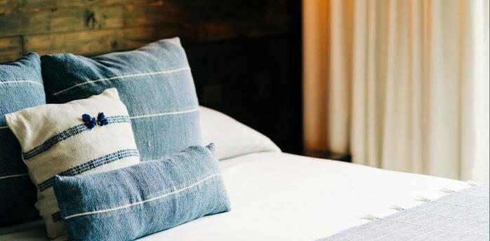A neatly arranged hotel room with soft lighting and blue-toned bedding