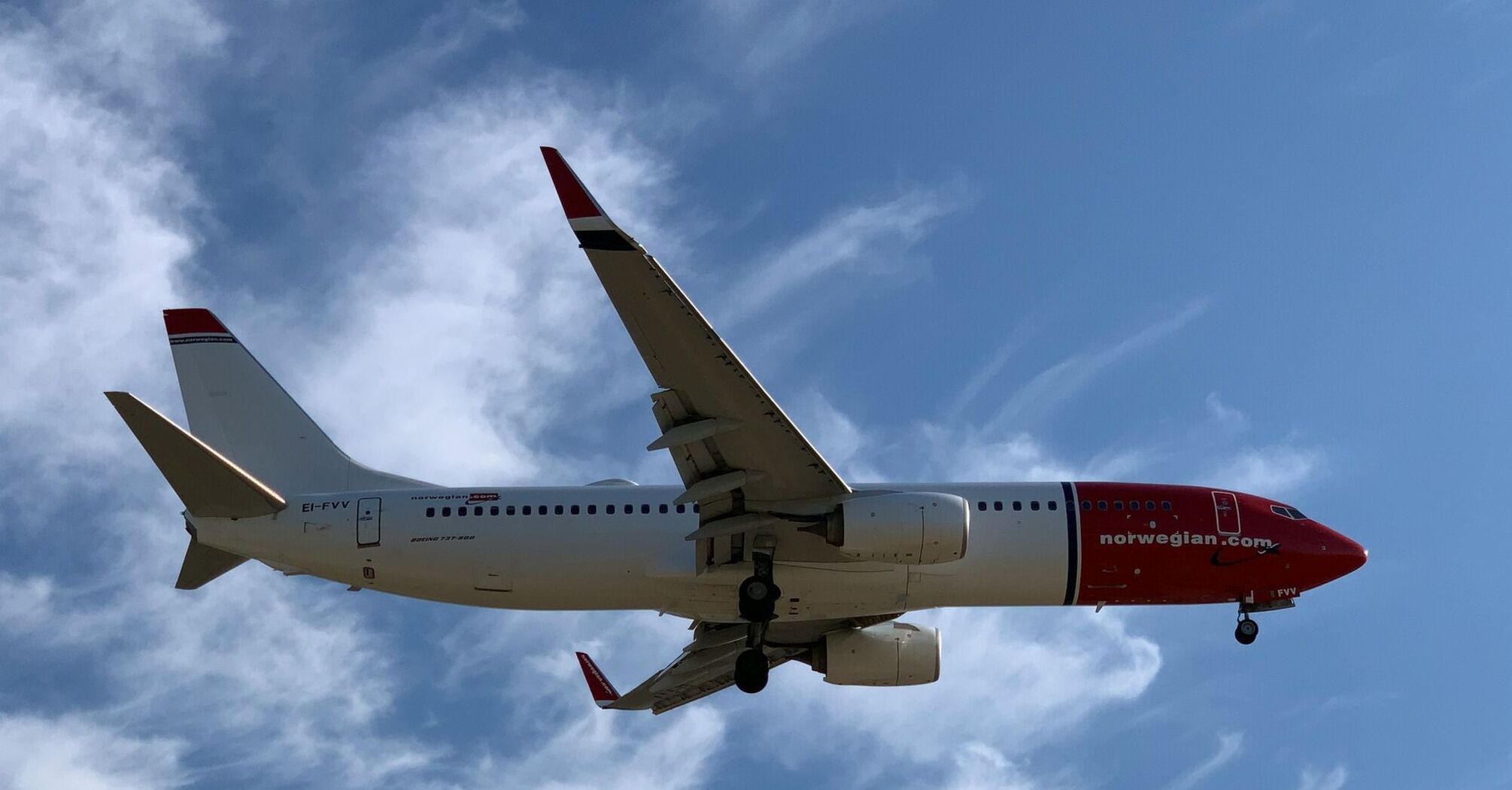 Norwegian aircraft approaching runway against blue sky