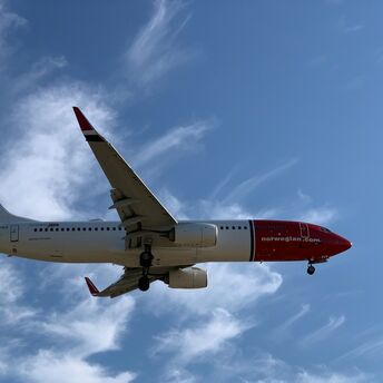 Norwegian aircraft approaching runway against blue sky