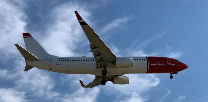 Norwegian aircraft approaching runway against blue sky