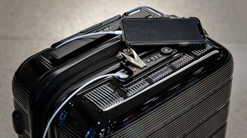 Smart suitcase with phone and charging cable placed on top at an airport