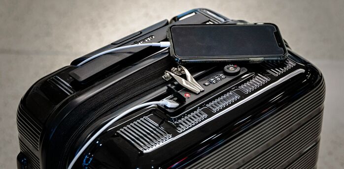Smart suitcase with phone and charging cable placed on top at an airport