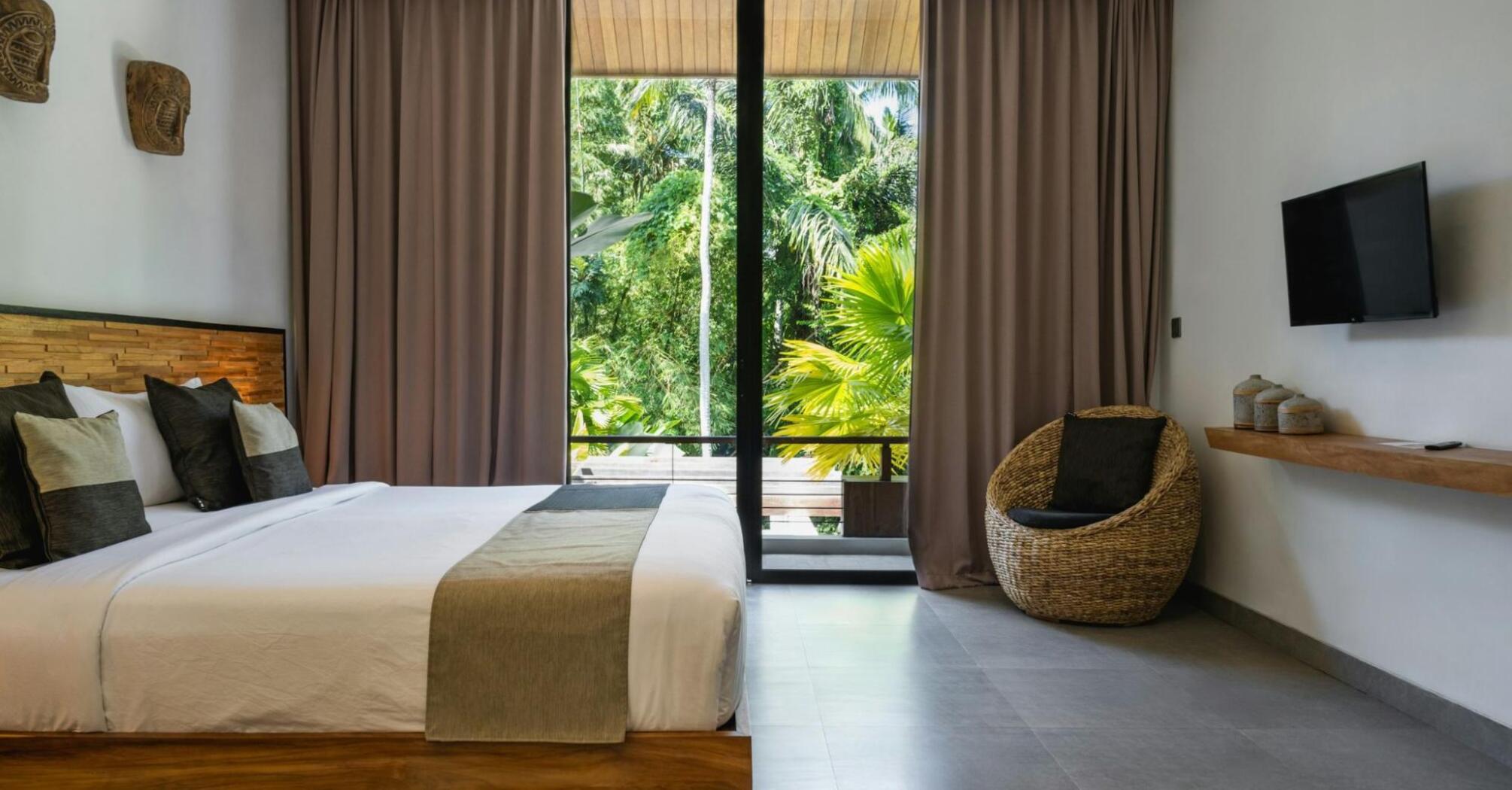 Modern hotel room with large windows overlooking tropical greenery