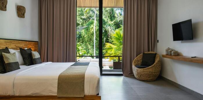 Modern hotel room with large windows overlooking tropical greenery