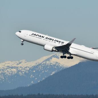 Japan Airlines aircraft taking off with snowy mountains in the background