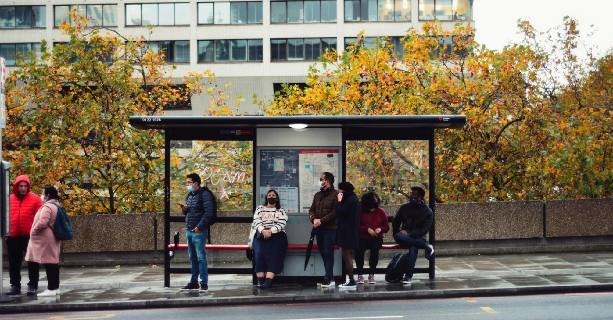 Passengers waiting at a London bus stop on a cloudy autumn day