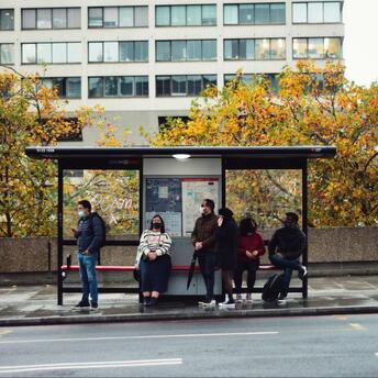 Passengers waiting at a London bus stop on a cloudy autumn day