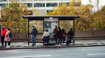 Passengers waiting at a London bus stop on a cloudy autumn day