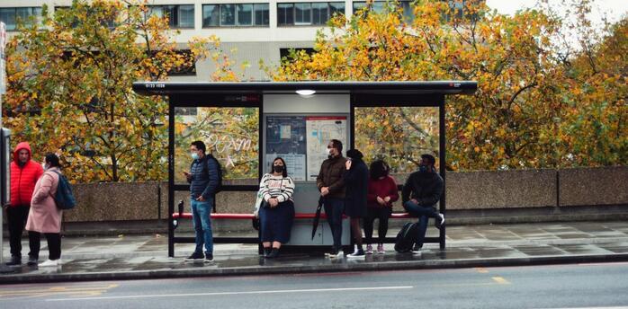 Passengers waiting at a London bus stop on a cloudy autumn day