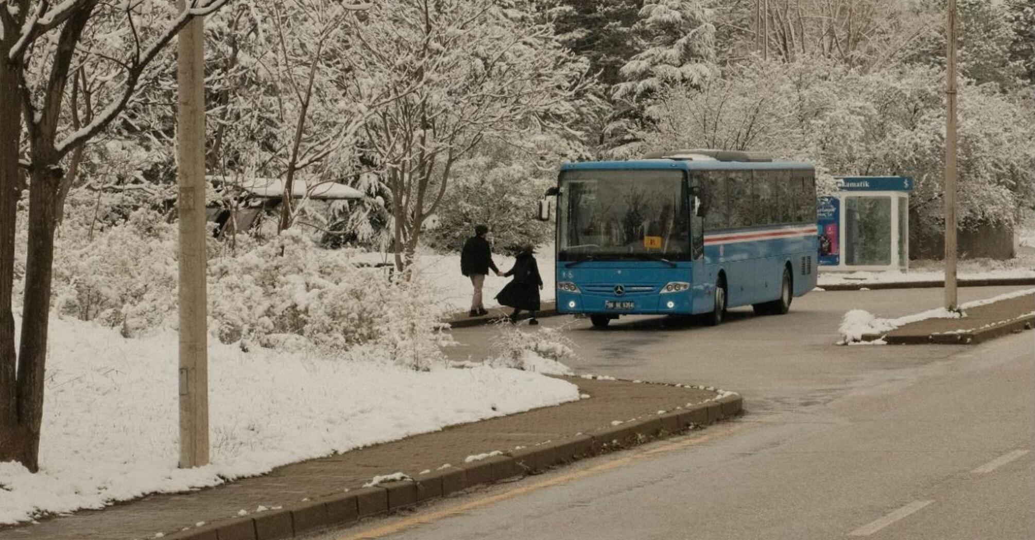 Blue bus arriving at a snowy roadside stop