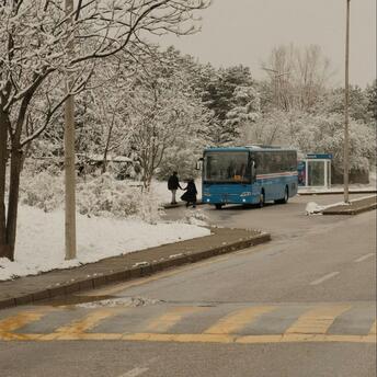 Blue bus arriving at a snowy roadside stop