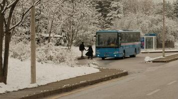 Blue bus arriving at a snowy roadside stop