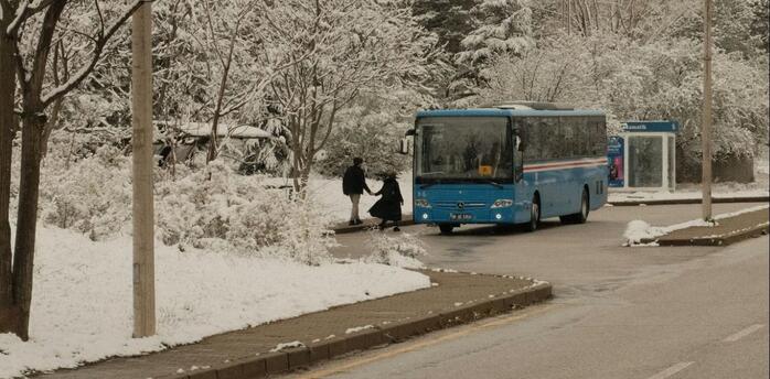 Blue bus arriving at a snowy roadside stop