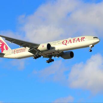 Qatar Airways aircraft approaching for landing against a blue sky