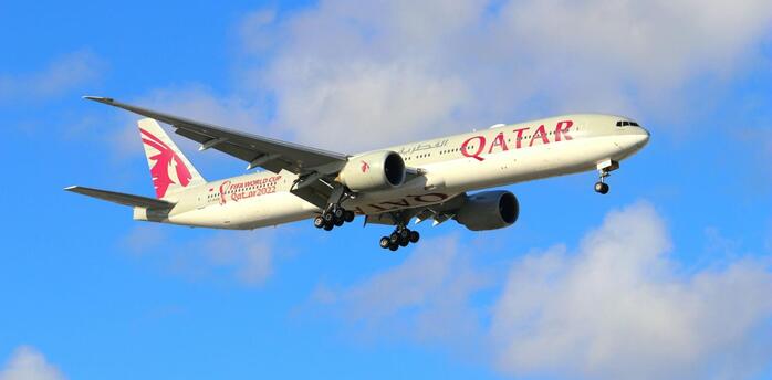 Qatar Airways aircraft approaching for landing against a blue sky