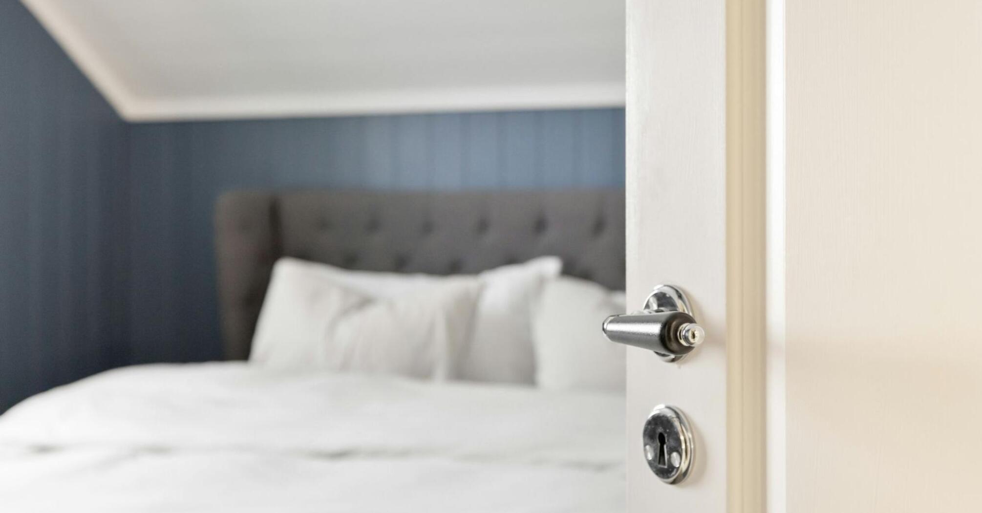 Open white door leading into a neatly made hotel bed