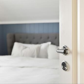 Open white door leading into a neatly made hotel bed