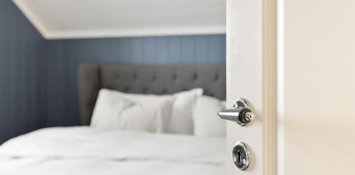 Open white door leading into a neatly made hotel bed