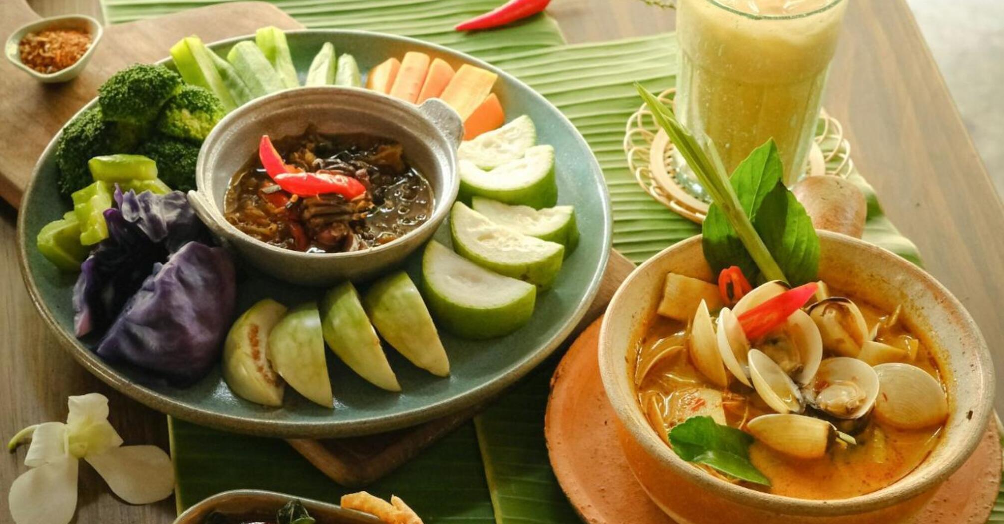 Traditional Thai dishes with fresh vegetables, seafood curry, and iced drink on a wooden table