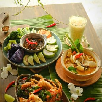Traditional Thai dishes with fresh vegetables, seafood curry, and iced drink on a wooden table