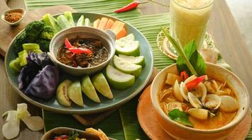 Traditional Thai dishes with fresh vegetables, seafood curry, and iced drink on a wooden table