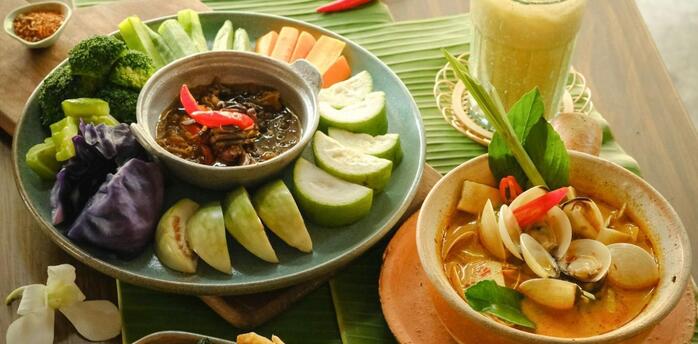 Traditional Thai dishes with fresh vegetables, seafood curry, and iced drink on a wooden table