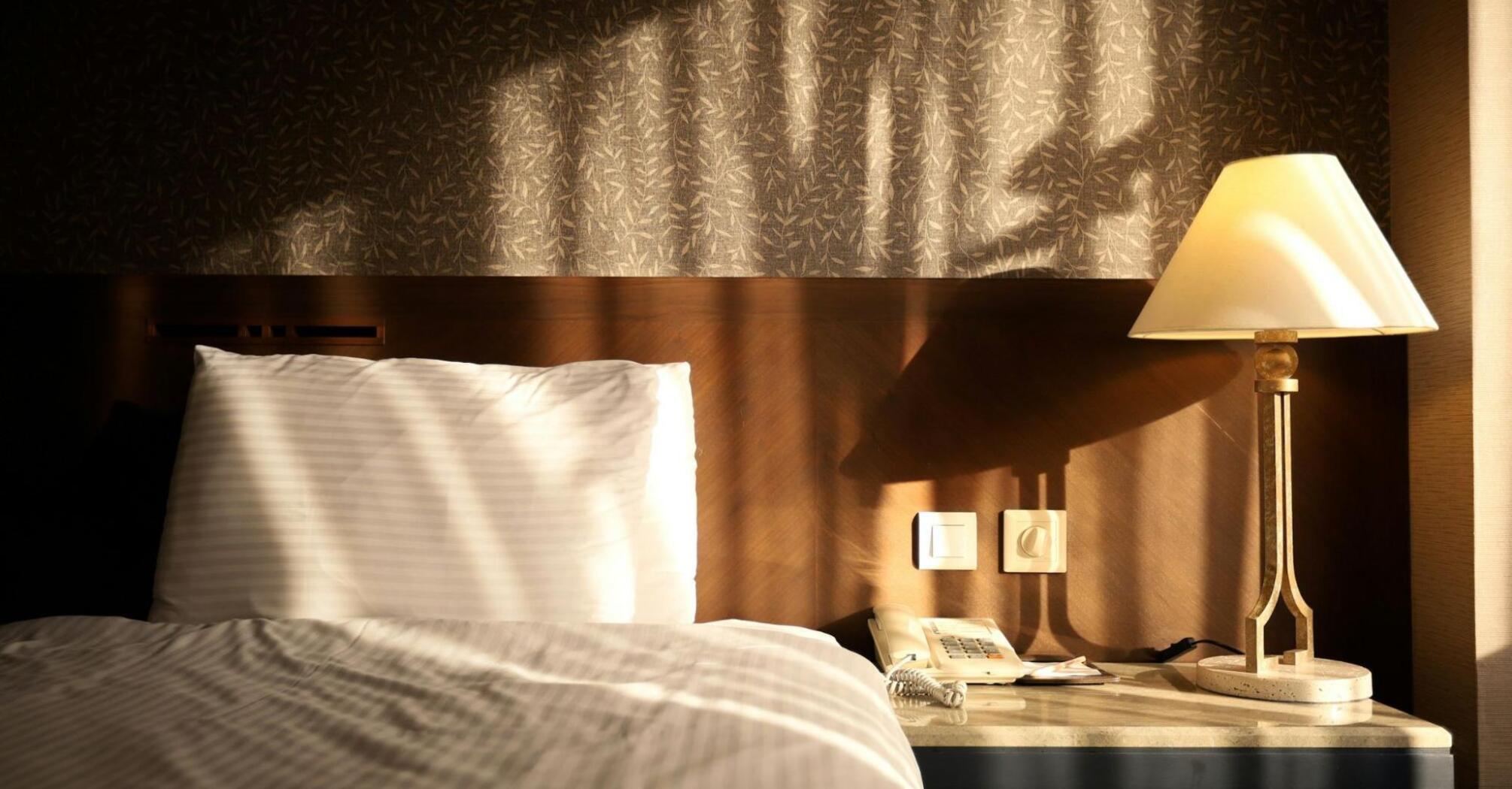 Sunlight falling on a hotel bed and bedside table with a lamp