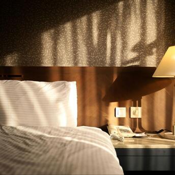 Sunlight falling on a hotel bed and bedside table with a lamp