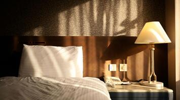 Sunlight falling on a hotel bed and bedside table with a lamp