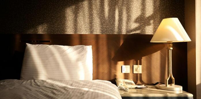 Sunlight falling on a hotel bed and bedside table with a lamp