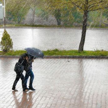 Travellers walking through heavy rain under an umbrella