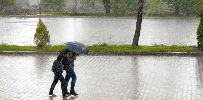 Travellers walking through heavy rain under an umbrella