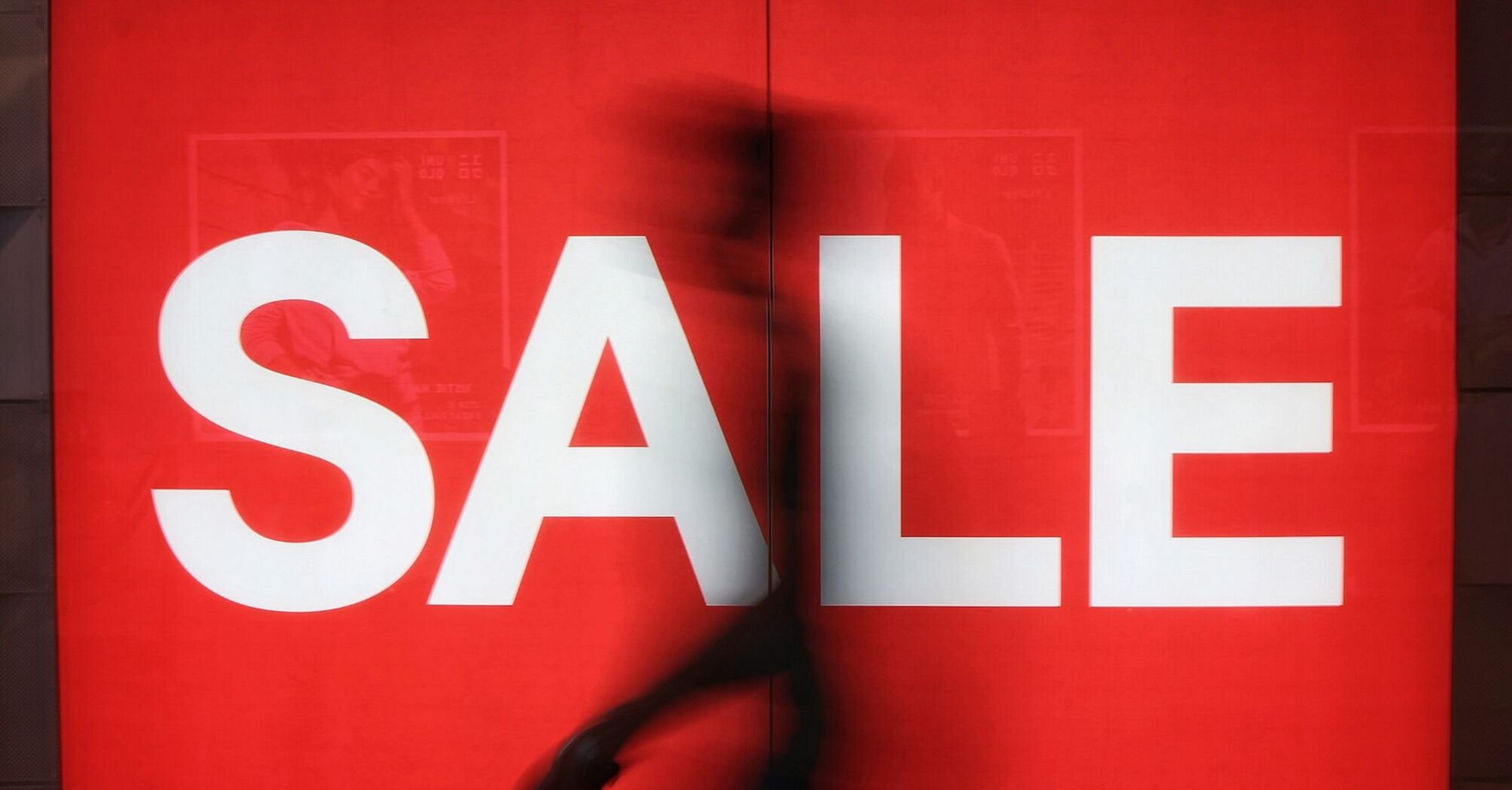 Large red sale sign with a blurred passer-by in front