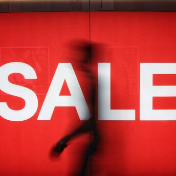 Large red sale sign with a blurred passer-by in front