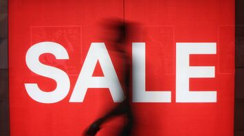 Large red sale sign with a blurred passer-by in front