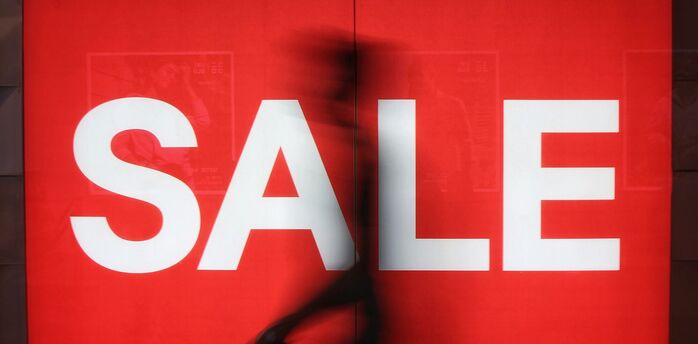 Large red sale sign with a blurred passer-by in front