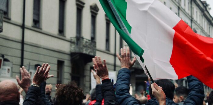 Crowd in Italy raising hands during public action with Italian flag