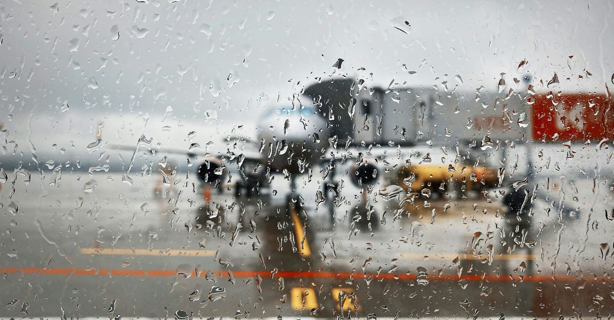 Rain-covered terminal window with aircraft visible on the tarmac