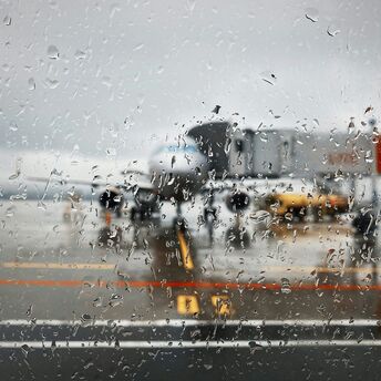 Rain-covered terminal window with aircraft visible on the tarmac