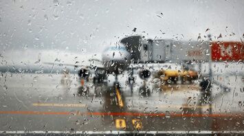 Rain-covered terminal window with aircraft visible on the tarmac